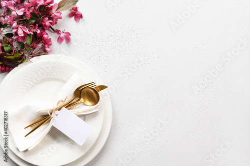 Spring elegance table setting with apple tree flowers, golden cutlery and tag on white table. View from above. Space for text.