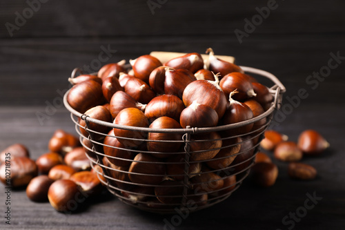 Fresh sweet edible chestnuts in basket on black table  closeup