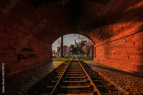 View from a tunnel. Historic train track in the park of Frankfurt on the river Ufer Main. Trees and meadow with flowers. Skyline of the financial district in the background
