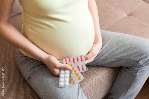 Midsection of pregnant woman taking vitamin pill on sofa at home
