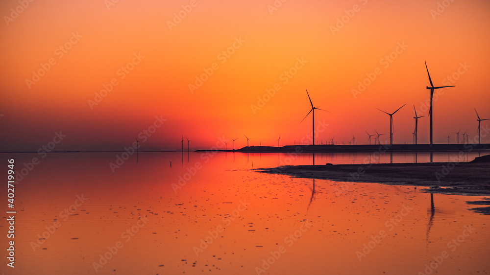 sunset on a pink lake, wind farms stand along the shore