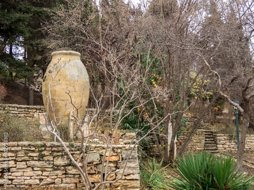 Big ceramic pot in the autumn botanical garden. Plants with autumn leaves around.