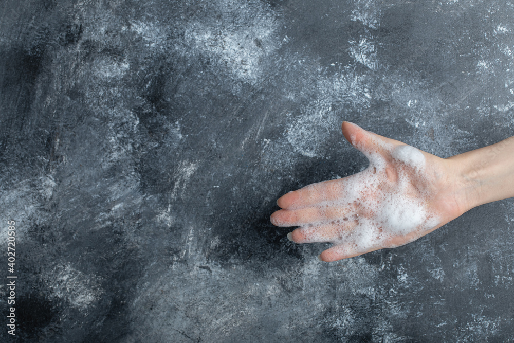 Fototapeta premium Hand with soap bubbles showing hand on marble background