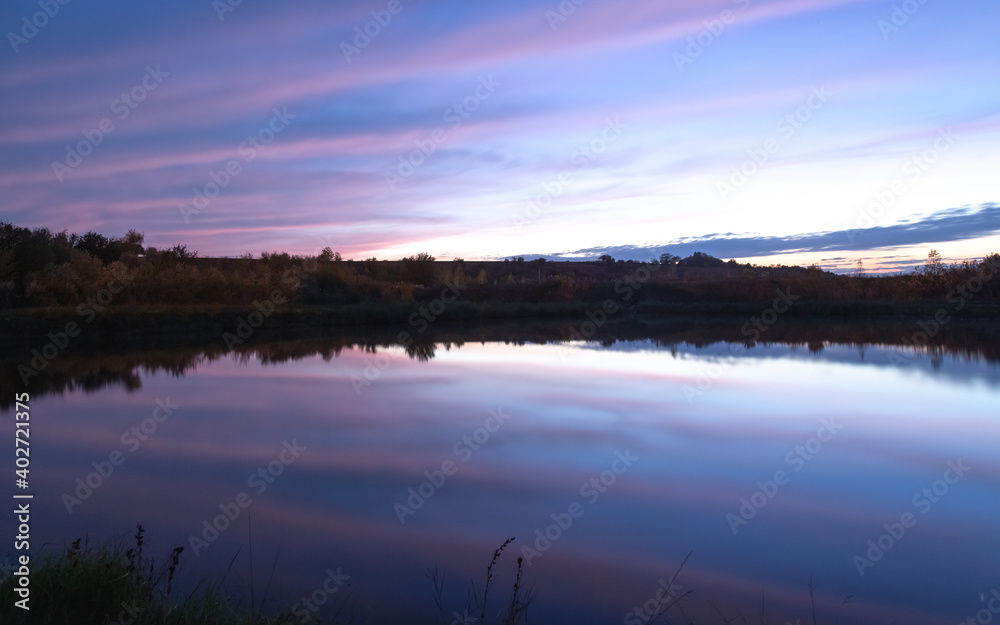 sunset over the river, the sky is reflected in the water, there is a small bridge on the river bank
