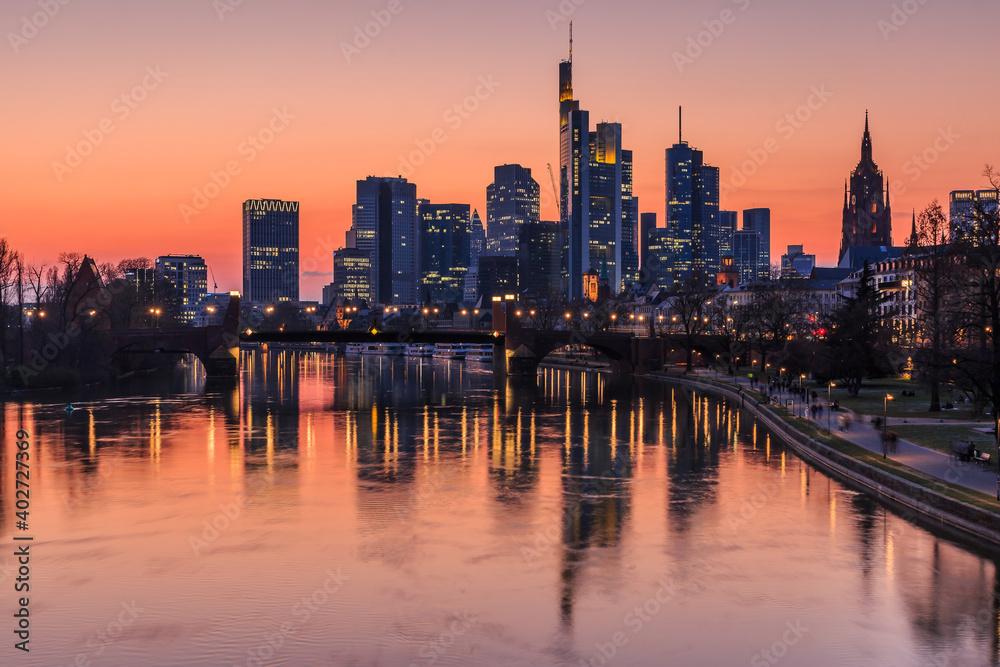 Frankfurt skyline in the evening. Sunset turns the sky orange-red. Reflections from illuminated houses from the financial district in the river Main