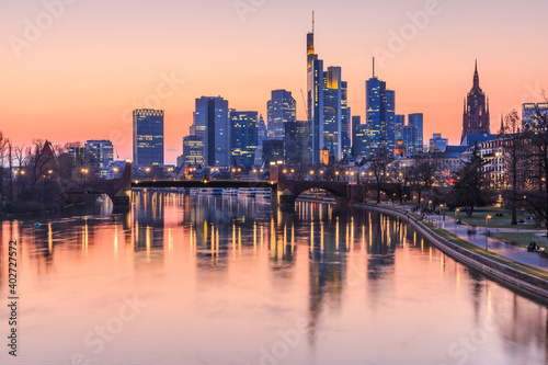 Frankfurt skyline in the evening. Commercial buildings from the financial district with lights and reflections in the water of the river Main at sunset. Bridge in the foreground.