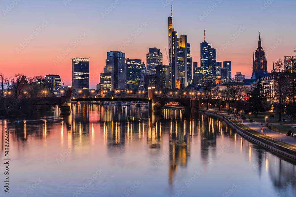 Frankfurt skyline in the evening at sunset. High-rise buildings from the financial district and river Main with reflections. Illuminated houses and bridge