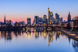 Frankfurt skyline in the evening. Sunset at blue hour with illuminated skyscrapers from the financial and business district. Reflections on the river Main with park on the bank
