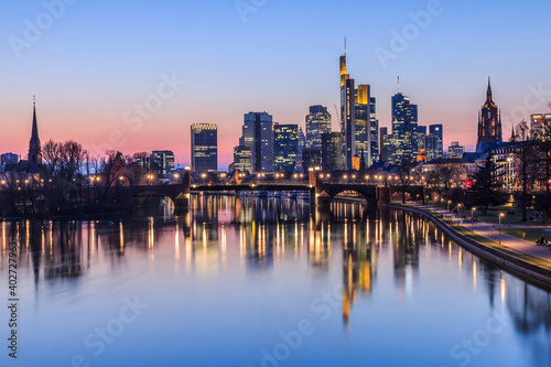 Frankfurt skyline in the evening. Sunset at blue hour with illuminated skyscrapers from the financial and business district. Reflections on the river Main with park on the bank