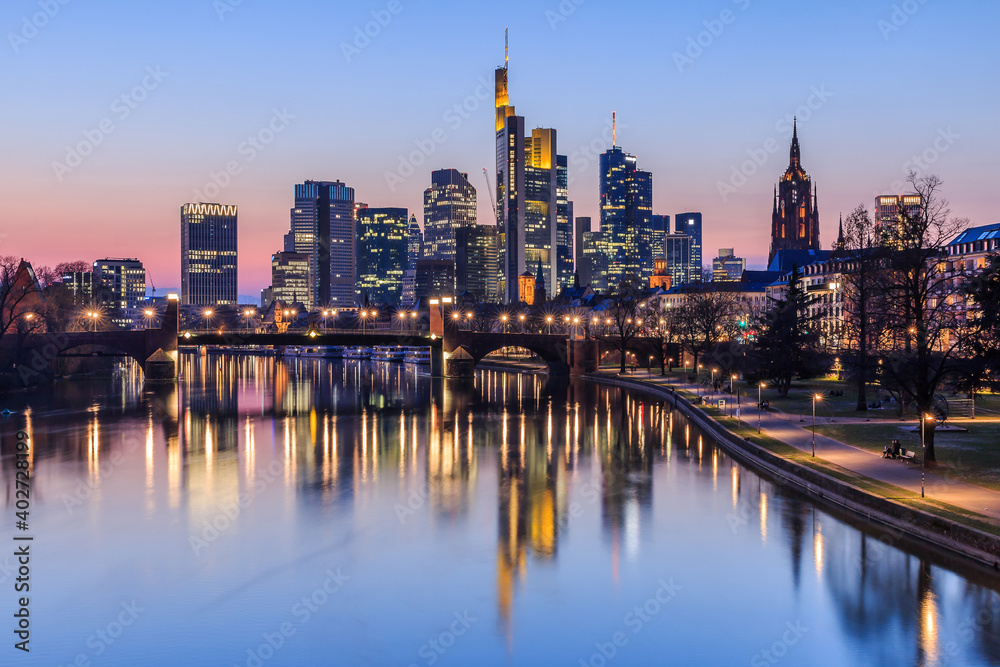 Frankfurt city skyline in the evening after sunset. Illuminated buildings of high-rise buildings from the business and financial center. Bridge over the river Main with street lights