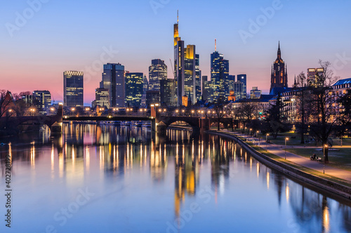 Frankfurt city skyline in the evening after sunset. Illuminated buildings of high-rise buildings from the business and financial center. Bridge over the river Main with street lights