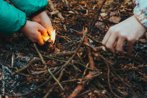 Obraz na plátně Children's hands light fire to fire in forest with lighter