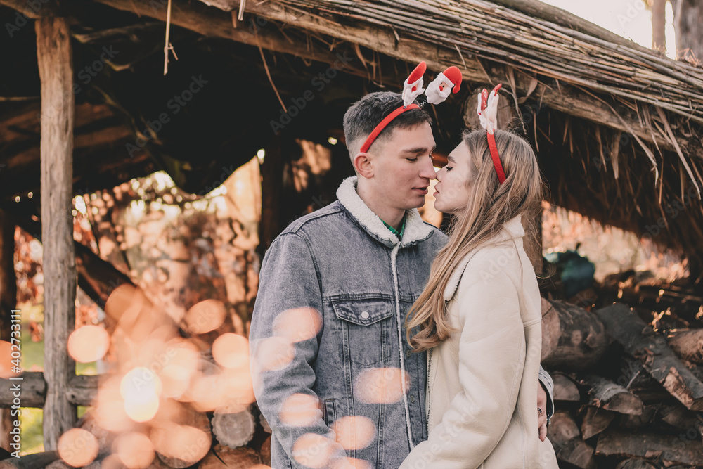 A couple dressed in New Year's hoops on their heads kissing on the background of a gazebo made of firewood
