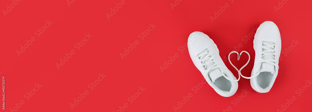 White sports shoes and heart shape from laces on a red background. Simple flat lay with copy space. - obrazy, fototapety, plakaty 