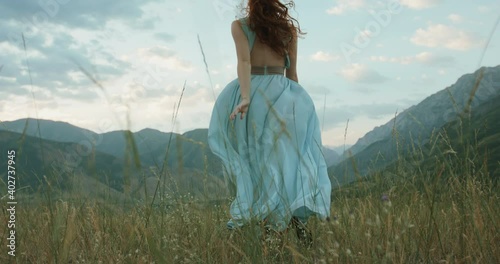 Woman in white dress running on a mountain with raised hands while wind is blowing her dress and red hair - freedom, nature concept 4k footage