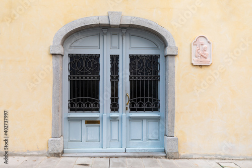 Porta chiusa molto vecchia su facciata di muro giallo con bassorilievo di gesu che porta il crocifisso.