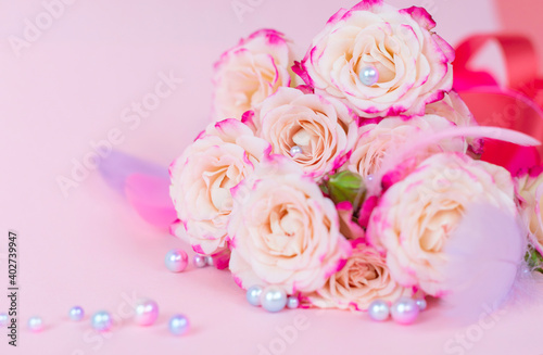 delicate bouquet of bushy peony roses with bright ribbons, pearls, feathers and hearts on a pink background, the concept of congratulations on Valentine's day