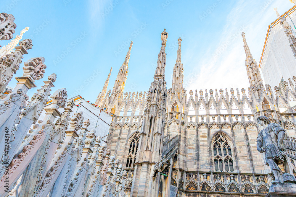 Roof of Milan Cathedral Duomo di Milano with Gothic spires and white marble statues. Top tourist attraction on piazza in Milan, Lombardia, Italy. Wide angle view of old Gothic architecture and art