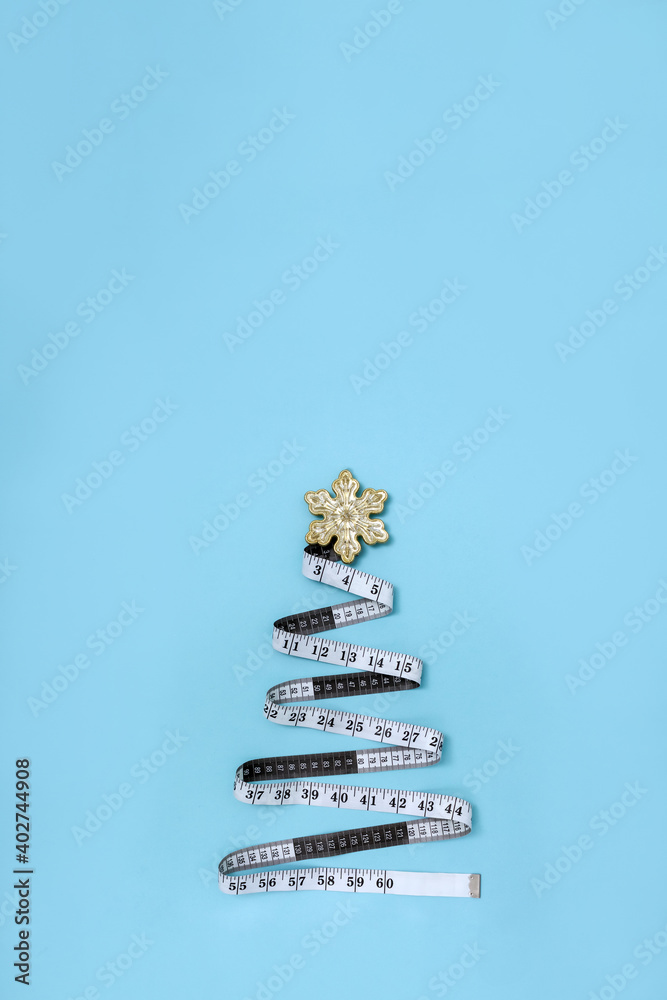 Measuring tape in the form of Christmas tree and New Year's toy on light blue background. Minimal concept of balanced diet for holidays. Vertical poster. Copy space Measuring tape in the form of Christmas tree and New Year's toy on light blue background. Minimal concept of balanced diet for holidays. Vertical poster. Copy space