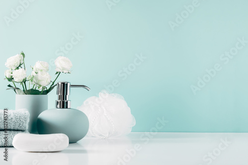 Foto Soft light bathroom decor in mint color, towel, soap dispenser, white roses flowers, accessories on pastel mint background