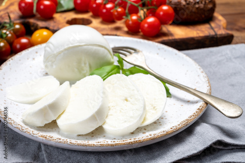 Cheese collection, eating. of white soft Italian cheese mozzarella, served with red cherry tomatoes, fresh basil leaves
