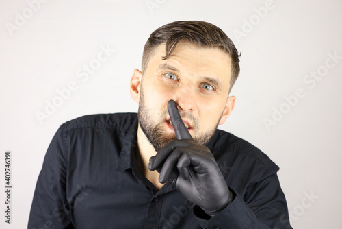 a man wearing medical gloves puts his index finger to his lips and makes a quiet gesture