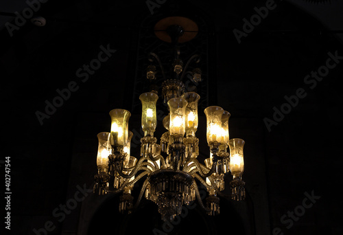 Crystal chandelier lamp with dim light in mosque. Decorative elegant chandelier, luxury retro style on dark background. Selective focus.