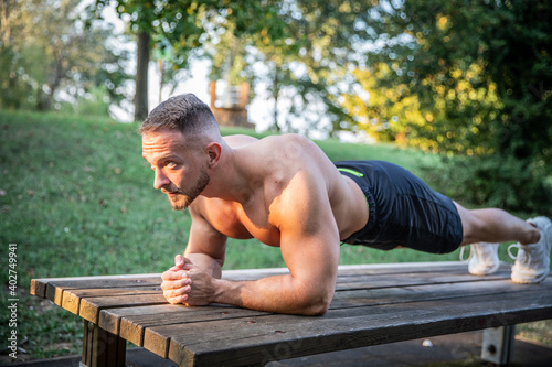 Athletic fit white man stands in plank pose. Outdoor workout in a park