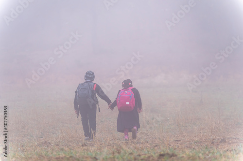 Two poor students go to school together in foggy weather