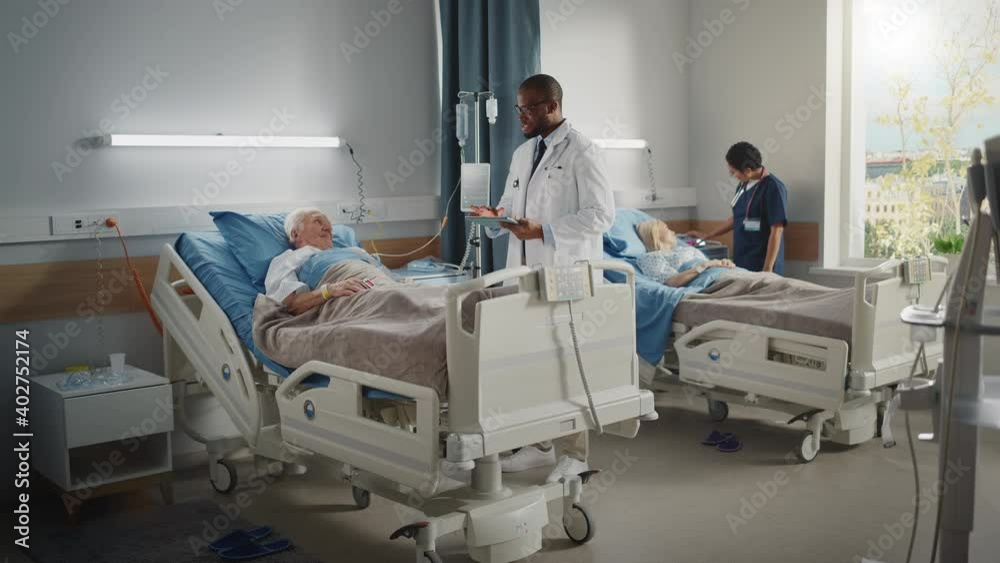 Hospital Ward: Friendly Doctor Asks Health Care Questions of Elderly Patient Resting in Bed. Physician Uses Tablet Computer, Does Checkup, Talks. Old Man Fully Recovering after Successful Surgery Hospital Ward: Friendly Doctor Asks Health Care Questions of Elderly Patient Resting in Bed. Physician Uses Tablet Computer, Does Checkup, Talks. Old Man Fully Recovering after Successful Surgery