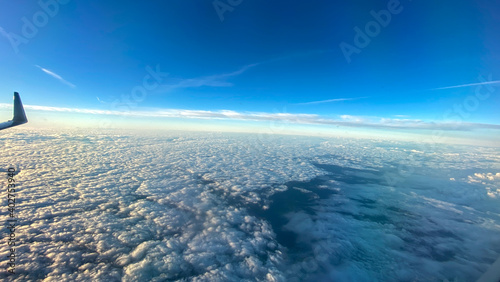 An aerial view from an airplane window of clouds with blue skies.