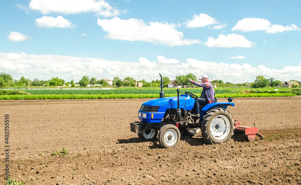 Obraz premium A farmer on a tractor with a mill unit crushes and processes the soil for further sowing with agricultural crops. Loosening surface, land cultivation. Plowing field. Use of agricultural machinery