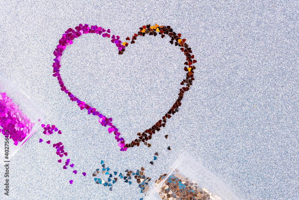 Heart shape made of multicolored glitter. Two champagne glasses with splash of heart shaped confetti over ultimate gray glitter background. Valentine's Day concept. Copy space. Top view