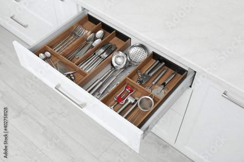 Billede på lærred Open drawer with different utensils and cutlery in kitchen, above view