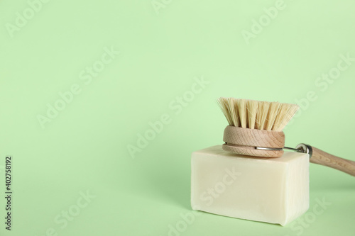 Cleaning brush and soap bar on green background  space for text. Dish washing supplies