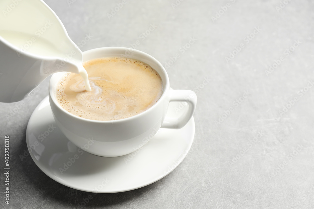 Pouring milk into cup of hot coffee on grey table, space for text Pouring milk into cup of hot coffee on grey table, space for text