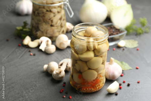 Glass jar of pickled mushrooms and ingredients on grey table. Space for text