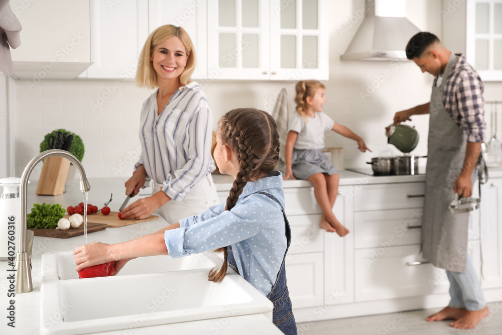 Little girl with her mother washing vegetables together in modern kitchen Little girl with her mother washing vegetables together in modern kitchen