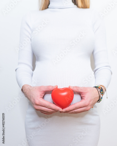 pregnancy, motherhood, people, love and expectation concept - close up of happy pregnant woman holding heart shape on her bare tummy