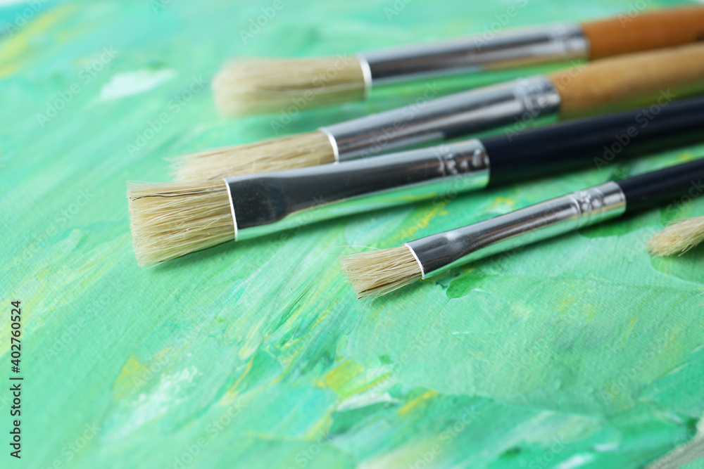 Fototapeta premium Set of different brushes on abstract colorful paint, closeup