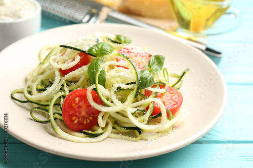 Delicious zucchini pasta with cherry tomatoes, basil and grated cheese served on light blue wooden table, closeup