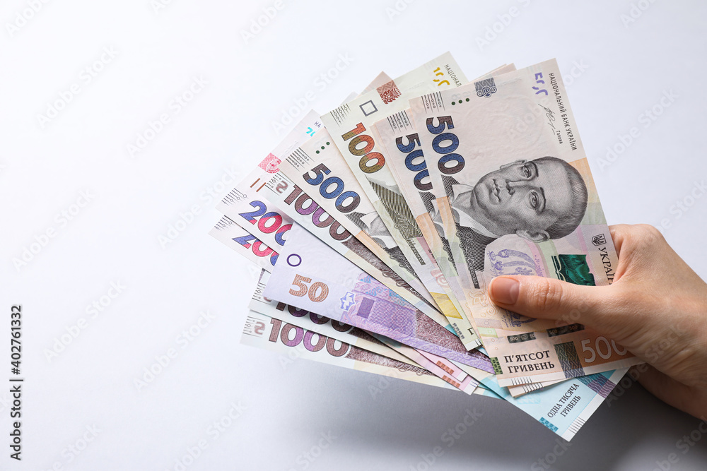 Woman holding Ukrainian money on light grey background, closeup Woman holding Ukrainian money on light grey background, closeup