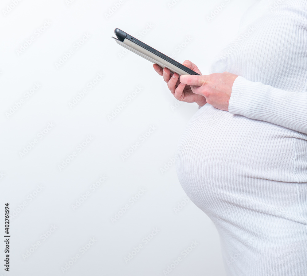 Content pregnant woman holding her tablet sitting on a couch in the living room at home Content pregnant woman holding her tablet sitting on a couch in the living room at home