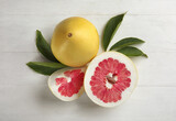 Fresh cut and whole pomelo fruits with leaves on white wooden table, flat lay