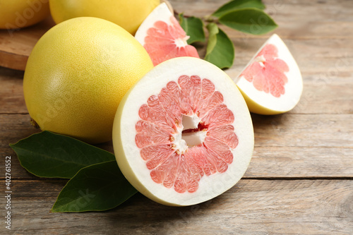 Fresh cut and whole pomelo fruits on wooden table, closeup photo