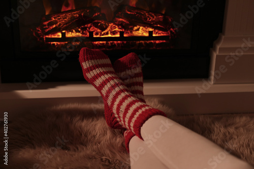 Woman in warm socks resting near fireplace with burning woods indoors, closeup