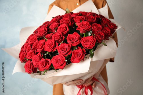 Fototapeta Naklejka Na Ścianę i Meble -  Woman holding luxury bouquet of fresh red roses on light background, closeup