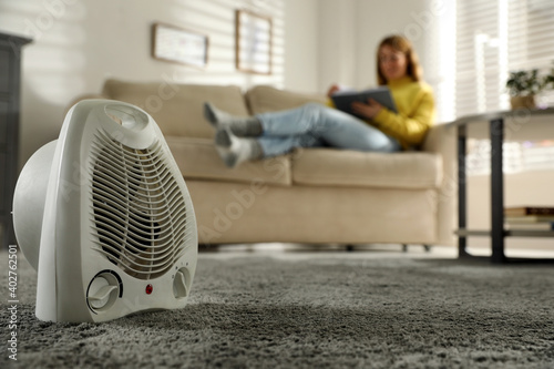 Schilderij op canvas Woman reading book in living room, focus on electric fan heater