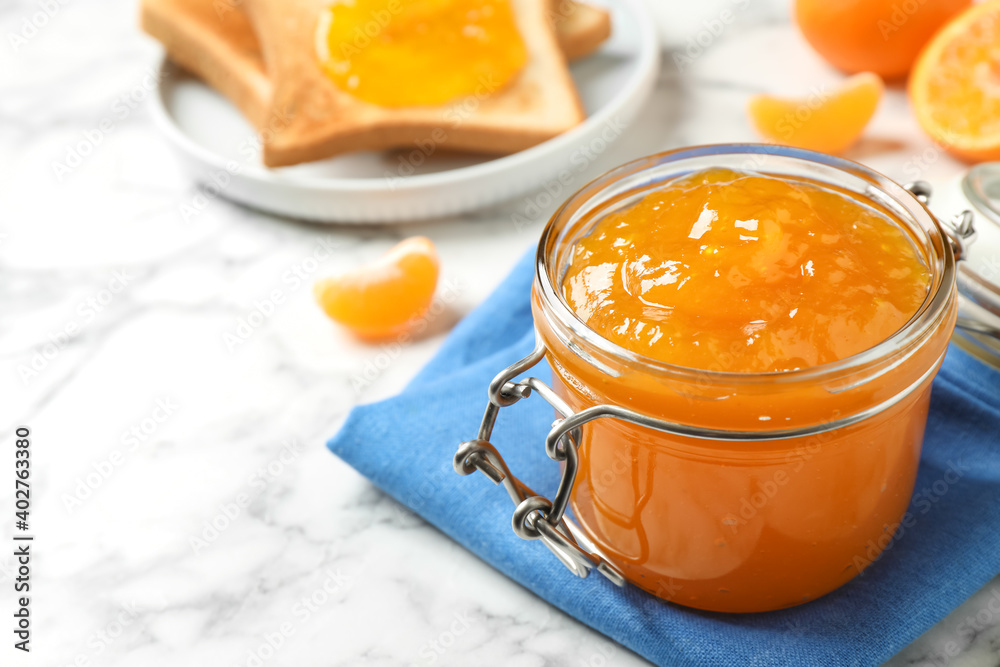 Tasty tangerine jam in glass jar on white marble table, space for text Tasty tangerine jam in glass jar on white marble table, space for text