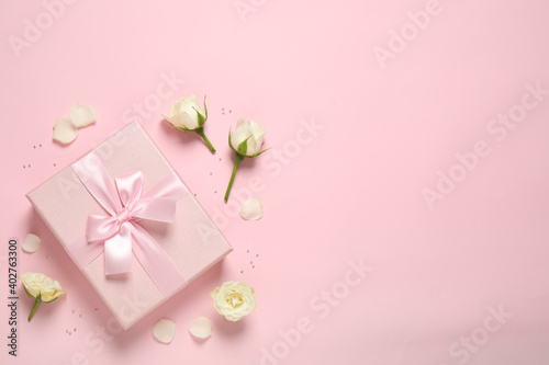 Elegant gift box and beautiful flowers on pink background, flat lay. Space for text